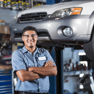 auto technician standing in front of a car on a lift with their arms crossed